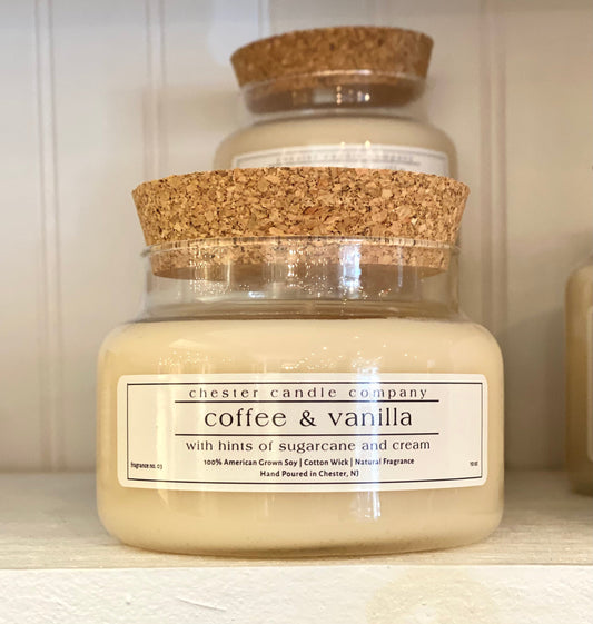 Natural Soy Wax Candle in a Clear Glass Apothecary-Style Jar and a Cork Lid. White Label on the Jar Reads "chester candle company. coffee & vanilla with hints of sugarcane and cream. 100% American Grown Soy, Cotton Wick, Natural Fragrance. Fragrance No. 03 Hand Poured in Chester, NJ. 10oz”